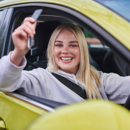 a blonde woman smiles out of the window of her new yellow car